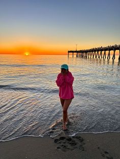 a woman standing on top of a sandy beach next to the ocean with a pier in the background