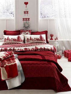 a bed with red and white comforters in a room next to two windows, decorated with christmas decorations