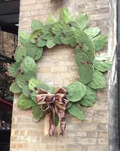 a wreath is hanging on the side of a brick building with green leaves and bows