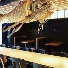 a large fish sculpture hanging from the ceiling in a room with wooden tables and chairs