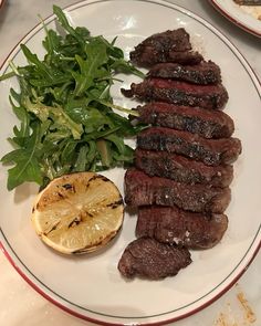 a plate with steak, lemon and spinach on it next to other food items