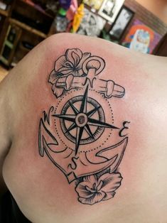 an anchor, compass and flower tattoo on the back of a woman's shoulder