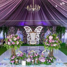 an elaborately decorated table with pink flowers and greenery in front of a purple drape