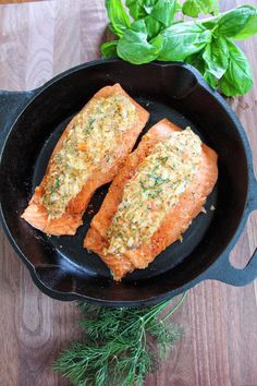 two salmon fillets in a cast iron skillet on a wooden table next to fresh herbs