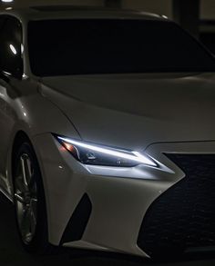 the front end of a white car with its lights on