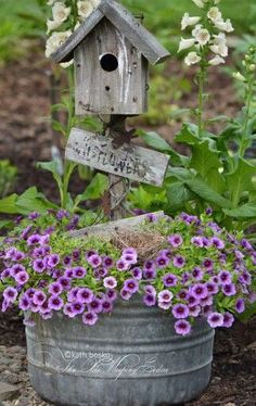 a birdhouse sitting on top of a metal bucket filled with purple flowers