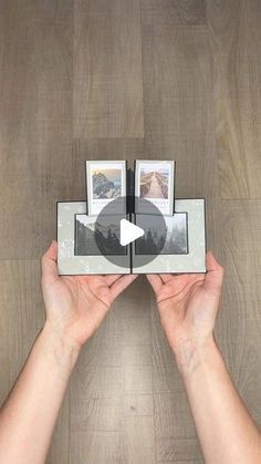 two hands holding an open photo frame with three pictures in it on a wooden floor