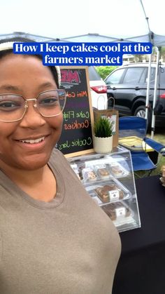 a woman wearing glasses standing in front of a sign that says how i keep cakes cool at the farmers market