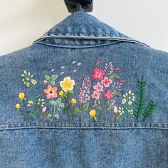 the back of a jean jacket with flowers embroidered on it and a black object in the background