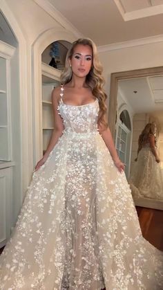 a woman standing in front of a mirror wearing a wedding dress with flowers on it