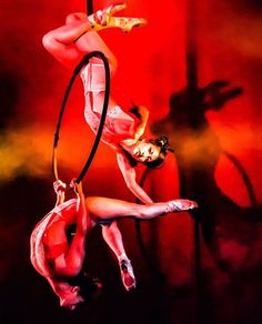 two women are performing aerial acrobatic tricks in front of a red background