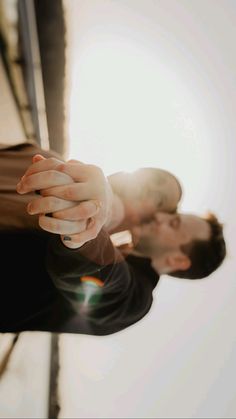 two people holding hands in front of a white wall with sunlight coming through the window