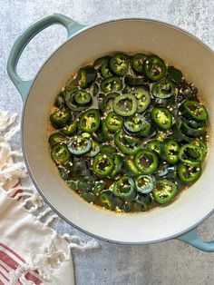 a pan filled with cooked green peppers on top of a white table cloth next to a red and white towel