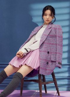 a woman sitting on top of a wooden chair wearing a pink skirt and blazer