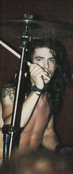 a shirtless man with long hair and tattoos holding a drumstick in his hand