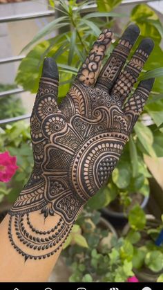 a hand with henna on it and some plants in the backgroung