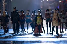 a group of people dressed in costumes standing on a street corner at night with lights behind them