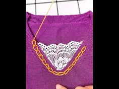 someone is stitching an embroidered triangle on a purple sweater with gold chains hanging from it