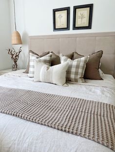 a bed with four pillows on it and two framed pictures above the bedspread