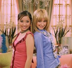 two young women standing next to each other in front of a living room filled with furniture