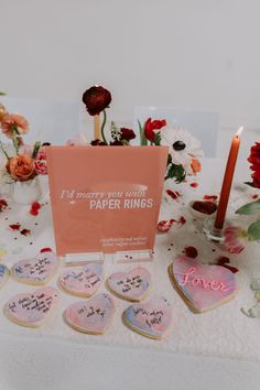 a table topped with lots of heart shaped cookies next to a lit candle and flowers