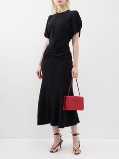 a woman wearing a black dress and holding a red handbag in front of her