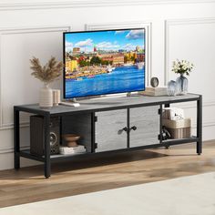 a flat screen tv sitting on top of a wooden table next to a vase with flowers