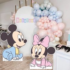 two mickey and minnie mouse cutouts on a table with balloons in the background