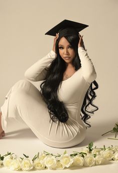 a woman sitting on the ground with her graduation cap over her head and flowers in front of her