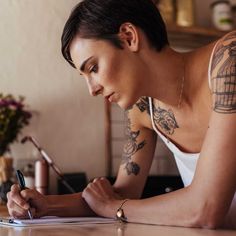 a woman sitting at a table writing on a piece of paper with a pen in her hand