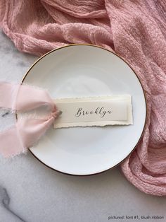 a plate with a name tag on it next to a pink scarf and a napkin