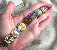 "You will receive this superb antique enamel Belgian souvenir bracelet. It measures 7 1/2\" x 3/4\" and is cast in an antiqued bronze tone base metal. The enamel on each panel is bright and intact. There are seven panels, Dinant, La Roche, Spa, Saint Hubert, Bastogne, Bruxelles, and Bouillon. This piece cam out of Belgium from my favorite antique store. It is in very good vintage condition with minimal signs of wear to the front and only slight ,metal loss on the back. Gorgeous. For finished vin Antique Enamel Bracelet Collectible, Souvenir Jewelry, Vintage Beads Necklace, Antique Store, Gold Wash, Enamel Bracelet, Dec 30, Rhinestone Bracelet, Antique Stores