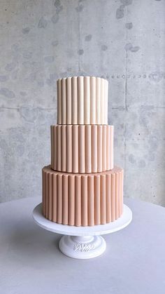 a three - tiered cake with pink icing sits on a white pedestal in front of a concrete wall