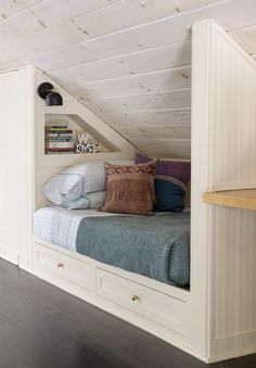 there is a bed in the attic with pillows on it and some bookshelves