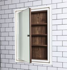 a white brick wall with a brown wooden cabinet in it's center and one door open