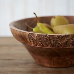 a wooden bowl filled with pears on top of a table