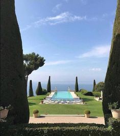 an outdoor swimming pool surrounded by hedges and trees with the ocean in the background on a sunny day