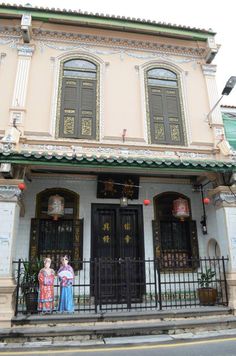 two people standing in front of a building with black doors and ornate iron railings