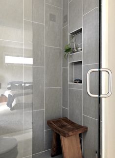 a bathroom with gray tiles and a wooden bench in the shower stall, next to a bed