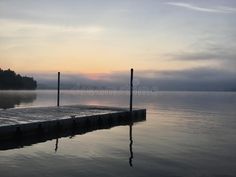 an empty dock in the middle of a lake at sunset with fog on the water