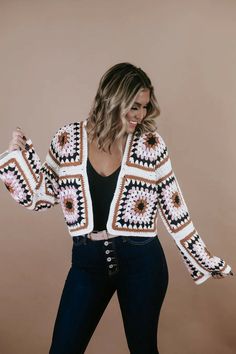 a woman wearing a crochet jacket and jeans, posing for the camera with her hands in her pockets