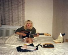 a woman sitting on top of a bed with an electric guitar