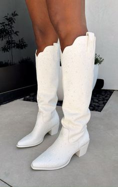 a woman in white boots standing on the ground with her legs crossed and wearing high heels