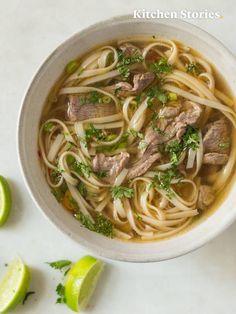 a white bowl filled with noodles and meat on top of a table next to limes