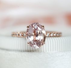 a pink diamond ring sitting on top of a white cloth