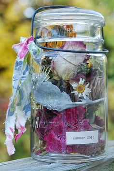 a jar filled with lots of flowers sitting on top of a wooden table next to a tree