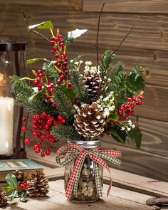 a vase filled with holly and pine cones on top of a table next to a candle