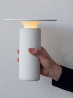 a person is holding a white light in front of a wall mounted lamp that has a dim light on it