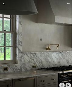 a kitchen with marble counter tops and stainless steel oven hoods, windows, and cabinets