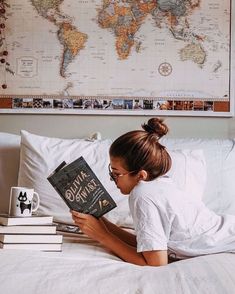 a woman laying in bed reading a book with a world map on the wall above her